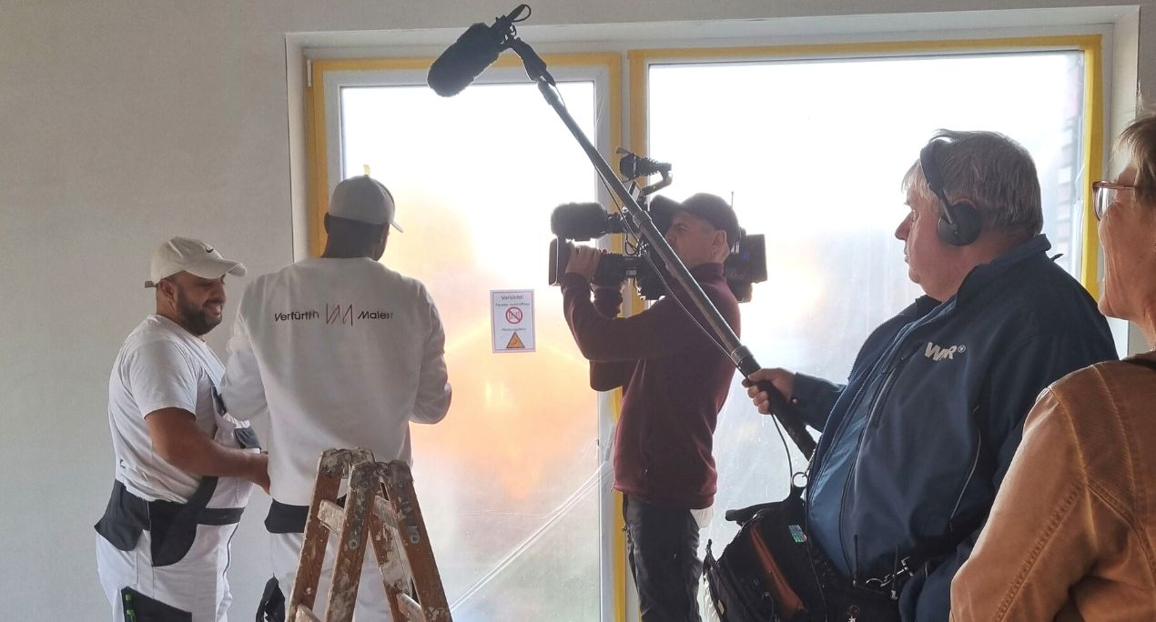 Fernsehteam filmt zwei Mitarbeiter bei der Arbeit auf der Baustelle