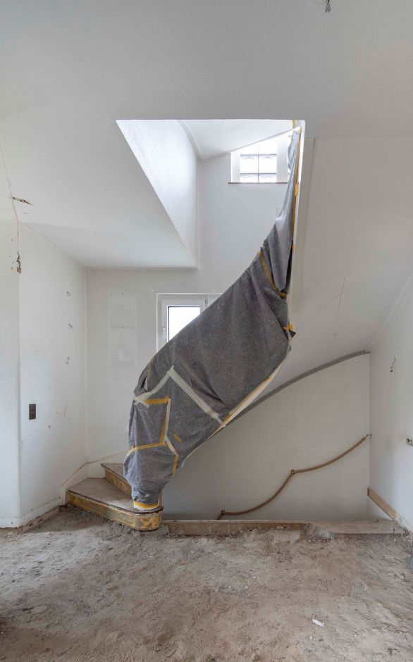 Vorher Aufnahme: Entkerntes Treppenhaus mit einem mit Malervlies abgedeckten Treppengeländer